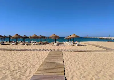 a sandy beach with umbrellas and chairs and the ocean at Apartamento frente ao mar com piscina de água salgada in Quarteira