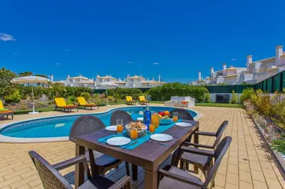 a wooden table with chairs next to a pool at Villa Gale Palm by Villa Plus in Albufeira
