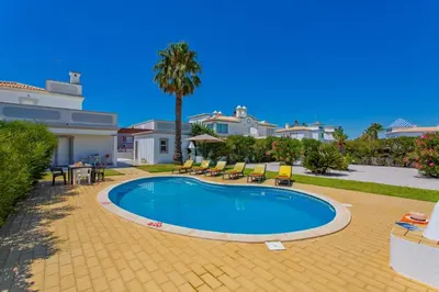 a swimming pool with chairs and a palm tree and houses at Villa Hope by Villa Plus in Galé