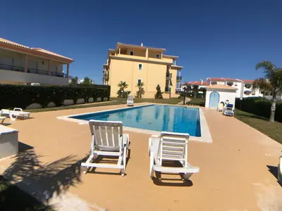 two lawn chairs and a swimming pool in front of a house at Oura Beach T1 apartment Coral , close to the Strip, Swimming Pool, Wi Fi, A/C in Albufeira