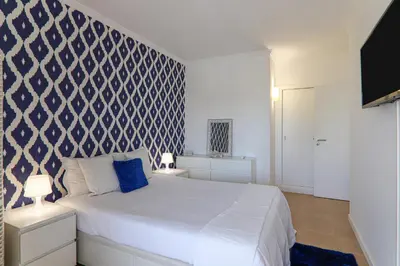 a bedroom with a white bed with a blue patterned wall at Refugio Salgados in Galé
