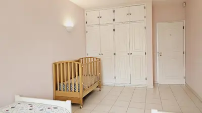 a room with a crib and white cabinets and a bedroom at Villa charmosa V3 junto à praia e à Marina de Vilamoura in Quarteira