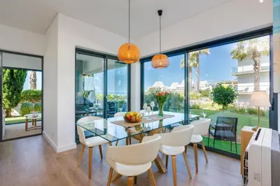 a dining room with a glass table and white chairs at Cavalo Preto Beach Residence with Garden & Pool in Quarteira