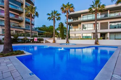 a swimming pool in front of a building with palm trees at Cavalo Preto Beach Residence with Garden & Pool in Quarteira