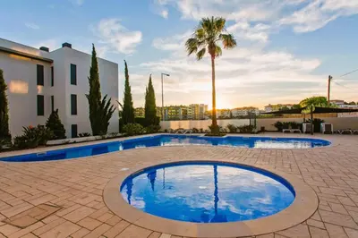 a pool in a courtyard with a palm tree and a building at Cavalo Preto Beach Residence with Garden & Pool in Quarteira