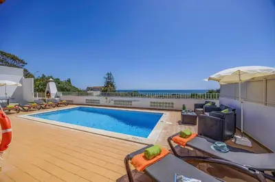 a swimming pool with chairs and an umbrella on a patio at Villa Marrachinho by Villa Plus in Albufeira