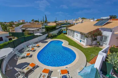 a swimming pool in a yard with chairs and a house at Villa Rocchi by Villa Plus in Albufeira