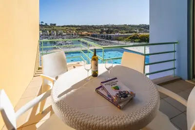 a table with a bottle of wine and a book on a balcony at Marina Breeze Apartment with Pool - 900m from the Beach in Albufeira