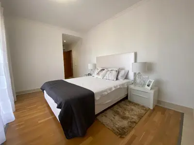a white bedroom with a large bed and a rug at V3 Vitória Boulevard in Vilamoura