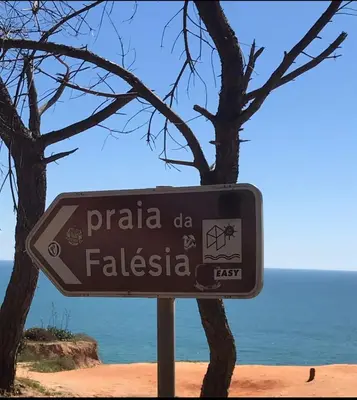 a sign in front of a tree next to the ocean at Falesia Beach Town house 2 bedroom in Olhos de Água