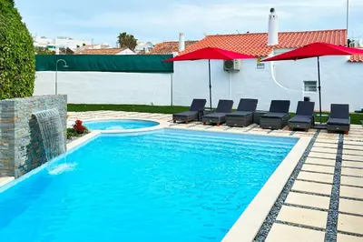 a swimming pool with chairs and umbrellas next to a house at LOTUS VILLA 2, ALBUFEIRA in Albufeira