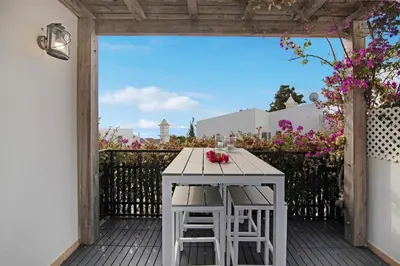 a table and two stools on a deck with flowers at Casa Estrela do Mar in Vale do Lobo
