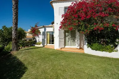 a white house with a yard with red flowers at Casa de Gales - Vilamoura in Vilamoura