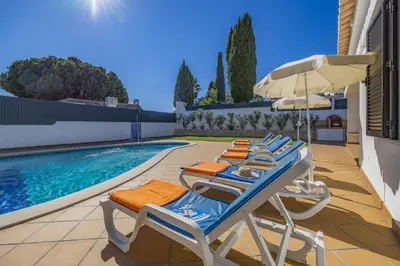 a row of lounge chairs and an umbrella next to a swimming pool at Villa Buganvillea by Villa Plus in Albufeira