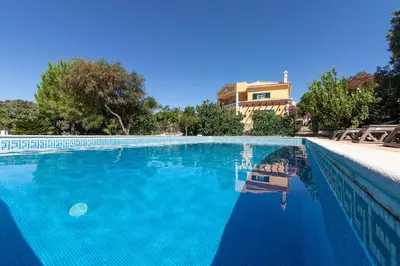 a large blue swimming pool with a house in the background at Monte das Palmeiras in Loulé