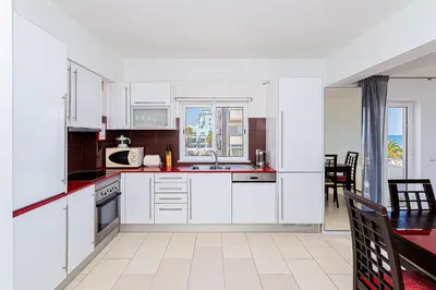 a kitchen with white cabinets and a dining room with a table at Frente praia SIM T3 Praia Quarteira by HsRentals in Quarteira