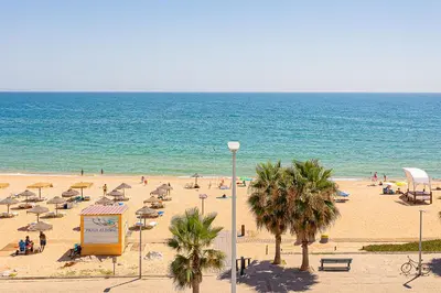 a beach with umbrellas and people on the beach at Frente praia SIM T3 Praia Quarteira by HsRentals in Quarteira