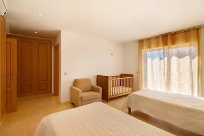 a bedroom with two beds and a chair and a crib at Casa Tulipas in Loulé