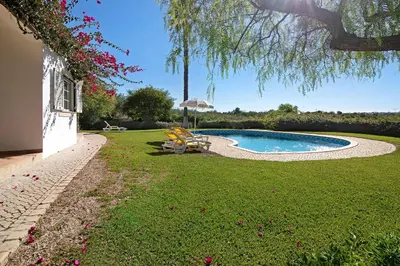 a yard with a swimming pool with chairs and an umbrella at Casa do Barrocal in Almancil