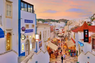 a group of people walking down a city street at AlbufeiraSun, arrive as a guest leave as a friend. in Albufeira