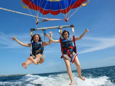 two girls are jumping in the water with a parachute at Lindo apartamento junto à praia e à Marina de Vilamoura com Piscina e Wi-Fi in Quarteira