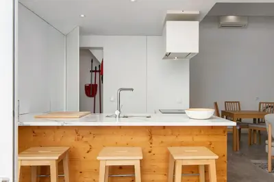 a kitchen with white cabinets and a counter with wooden stools at Casa Vermelha I in Faro