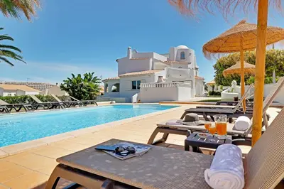a pool with chairs and umbrellas next to a house at Villux - Vila Enar-6 quartos, ideal para familias in Albufeira