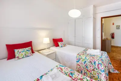two beds in a white room with red pillows at Apartamento Vista Mar T2 in Quarteira