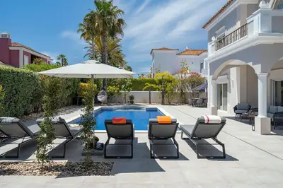 a patio with chairs and an umbrella next to a pool at Villa Flamingo - Quinta do Mar in Almancil
