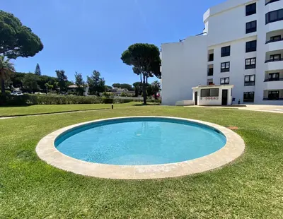 a swimming pool in the grass in front of a building at Ténis Studio Apartment - Vilamoura in Vilamoura