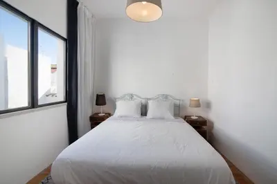 a bedroom with a white bed with two windows at Casa Loulé in Loulé