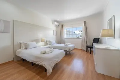 two beds in a room with white walls and wood floors at Villa Lemos by HelloVacations in Albufeira