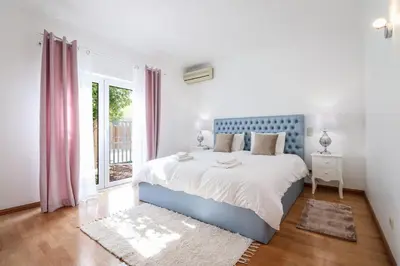 a white bedroom with a blue bed and a window at Villa Alfazema in Albufeira