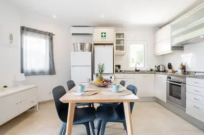a white kitchen with a wooden table and chairs at Villa at the beach in Vale do Lobo