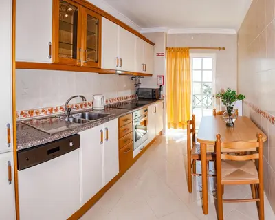 a kitchen with white cabinets and a wooden table at Tatiana 1 bedroom apartment in Albufeira