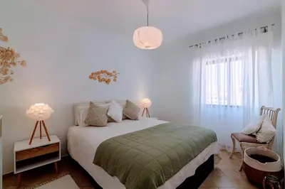 a white bedroom with a bed and a chair at Holiday 1 Bed Apartment with pool in Albufeira in Albufeira