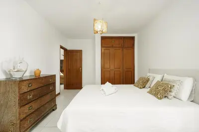 a white bedroom with a large bed and a dresser at APARTAMENTO TROPICANA in Quarteira