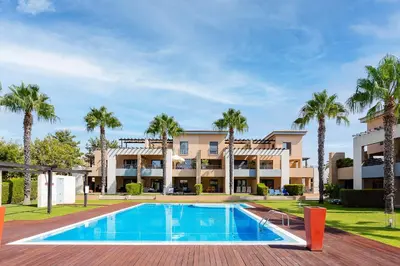 a villa with a swimming pool and palm trees at Apartamento Janelas Oceano - Vilamoura in Quarteira