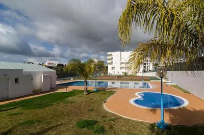 a swimming pool with a palm tree and a building at Albufeira Apartment Pool & Tennis in Albufeira