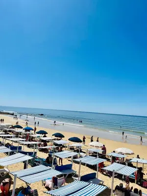 a beach with blue and white umbrellas and people at On The BEACH Stunning Apartment Albufeira Olhos de Água in Albufeira