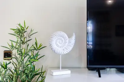 a white shell sculpture on a stand next to a plant at Golden Blue Beach Falésia Apartment in Albufeira