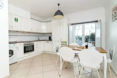 a kitchen with white cabinets and a table and chairs at Oura Sunrise 3F Apartment by Stay ici Algarve Holiday Rental in Albufeira