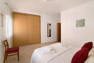 a bedroom with a white bed and a chair at Quarteira Beach iii in Quarteira