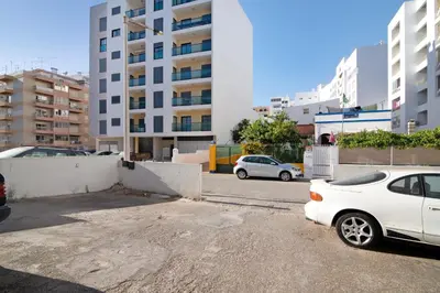 two white cars parked in a parking lot with buildings at Quarteira Beach I in Quarteira