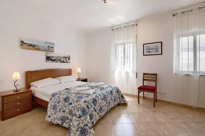 a bedroom with a bed and a chair and two windows at Quarteira Beach ii in Quarteira
