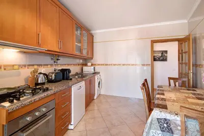 a kitchen with wooden cabinets and a table in it at Quarteira Beach ii in Quarteira