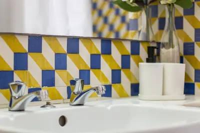 a bathroom sink with two faucets and a yellow and blue tiles at Casas Barulho - Villa Jacaranda A8 in Albufeira