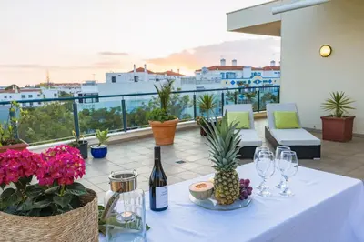 a table with wine glasses and flowers on a balcony at Penthouse Escape with Large Terrace, Pool & Garden in Quarteira