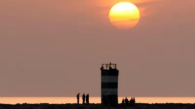 a group of people standing on a beach with a lighthouse at THE PALM at the Palm Village 2 Bedrooms Apartment in Vilamoura