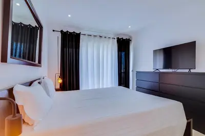 a bedroom with a white bed and a flat screen tv at AL - Quarteira Old Town in Quarteira